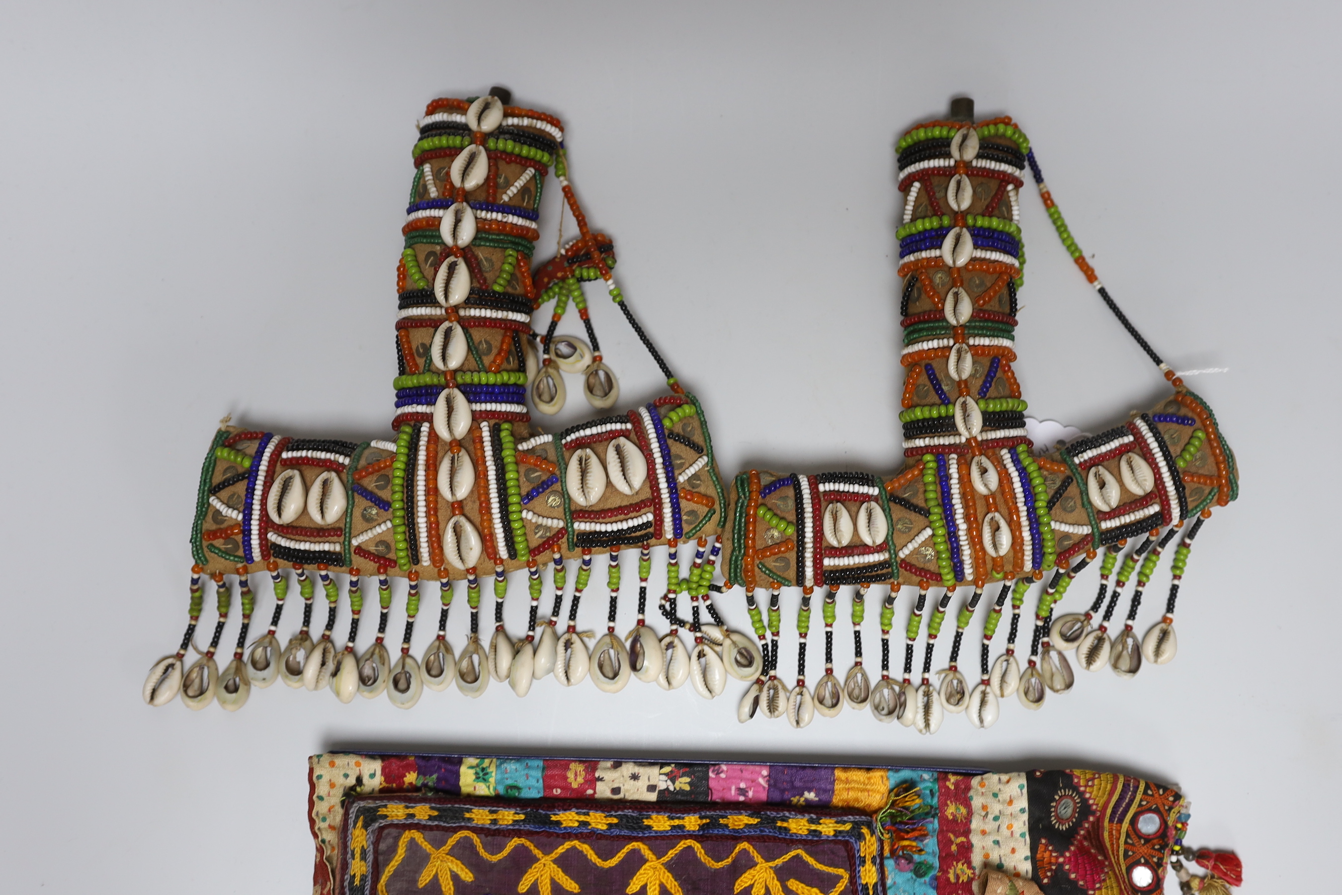 19th and 20th century textiles: An Indian mirrored and patchwork bag, a smaller embroidered bag, an ‘arrow’ shaped mirrored panel and two Omani shell and beaded ‘anchor’ shaped hangings, ‘arrow’ hanging 45cm long (5)